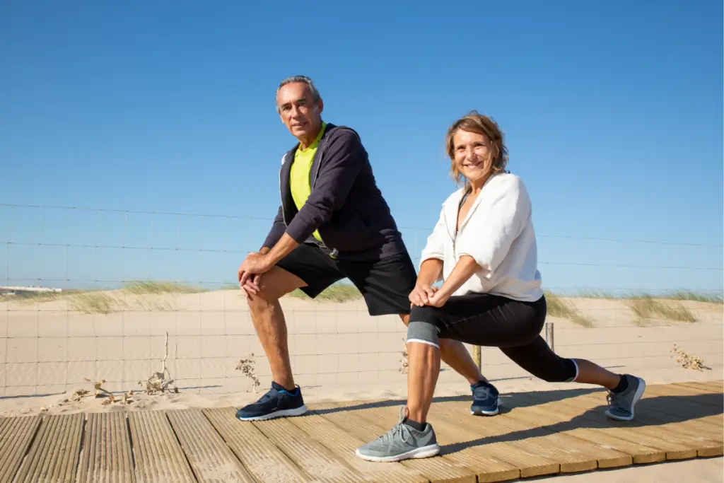 Two adults stretch outdoors near the beach.